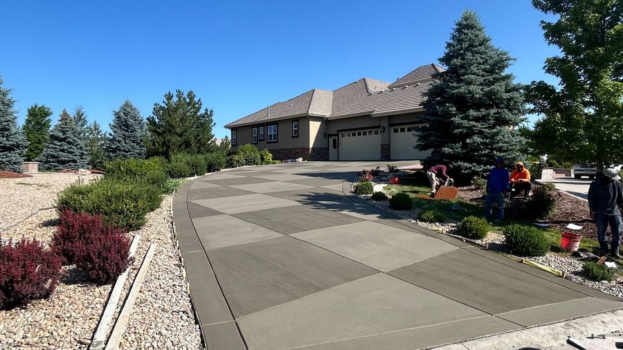 Freshly finished checkerboard-pattern concrete driveway leading to a modern stone-front home in Castle Rock