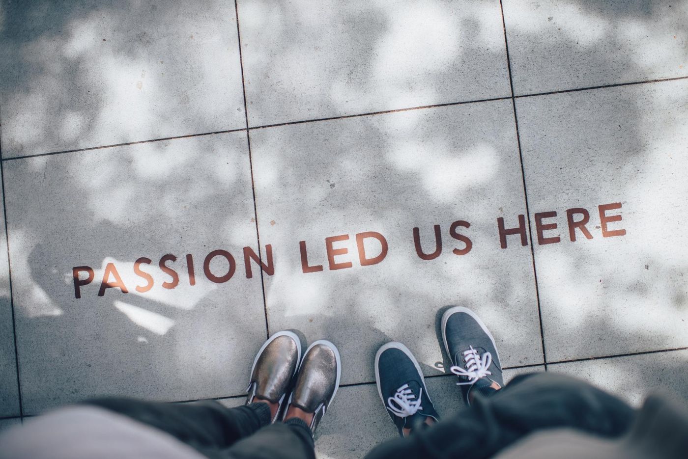 Two pairs of shoes on a concrete sidewalk beside the words “PASSION LED US HERE” painted in red