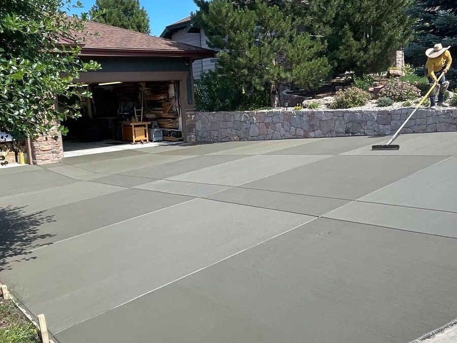 Freshly poured concrete driveway beside a house and stone wall, with trees in the background
