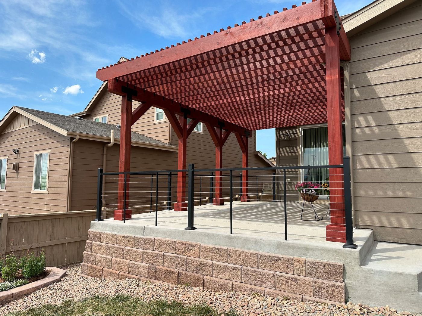 Covered backyard patio with red pergola roof, black railing, and concrete steps beside a house.