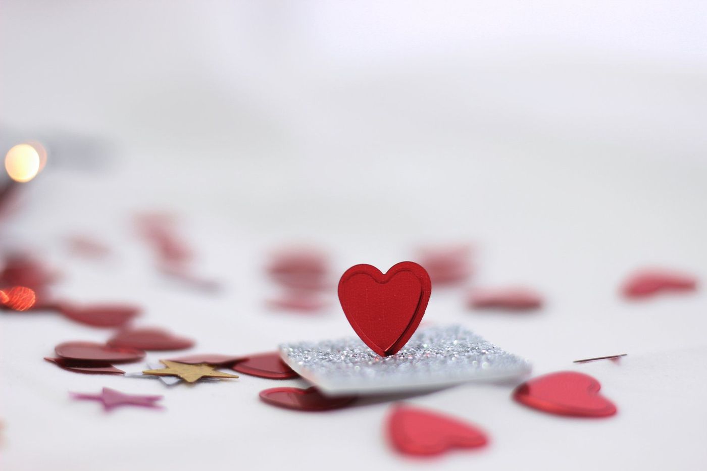 Small red heart on silver glitter with scattered red hearts on a white background