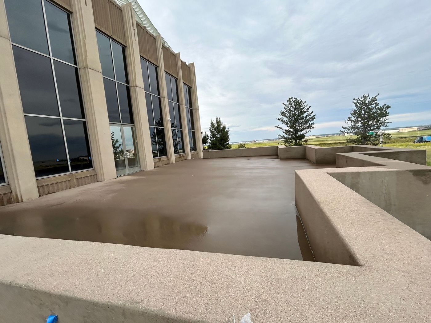 Modern building terrace with beige concrete walls, large windows, and cloudy sky over a distant landscape