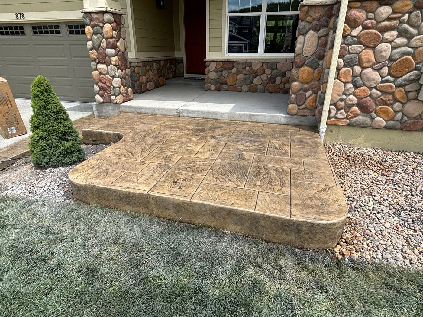 Front porch with stone facade and a small ramp leading to the entrance, bordered by gravel and a frosted lawn.