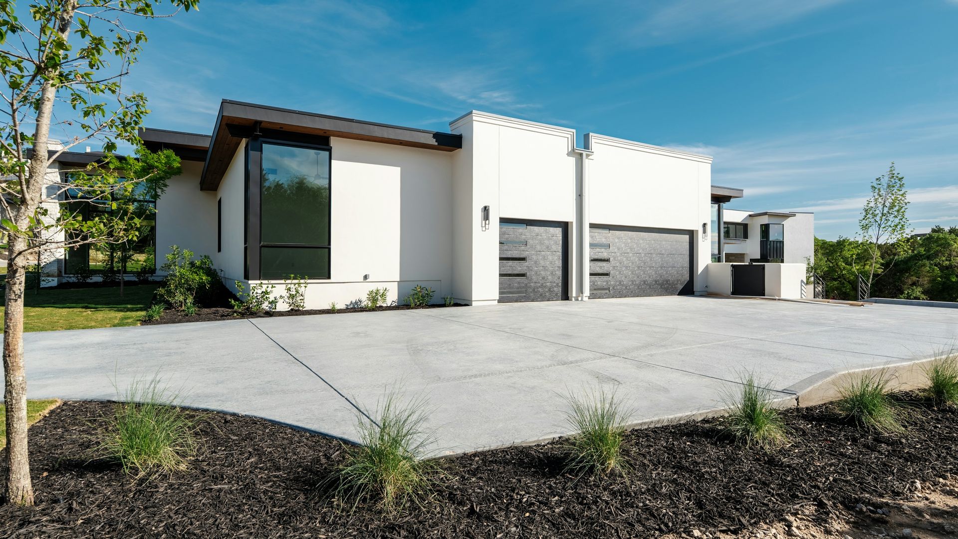 Light-gray concrete driveway in bright, direct sun outside a modern white home, the UV exposure that causes sun damage