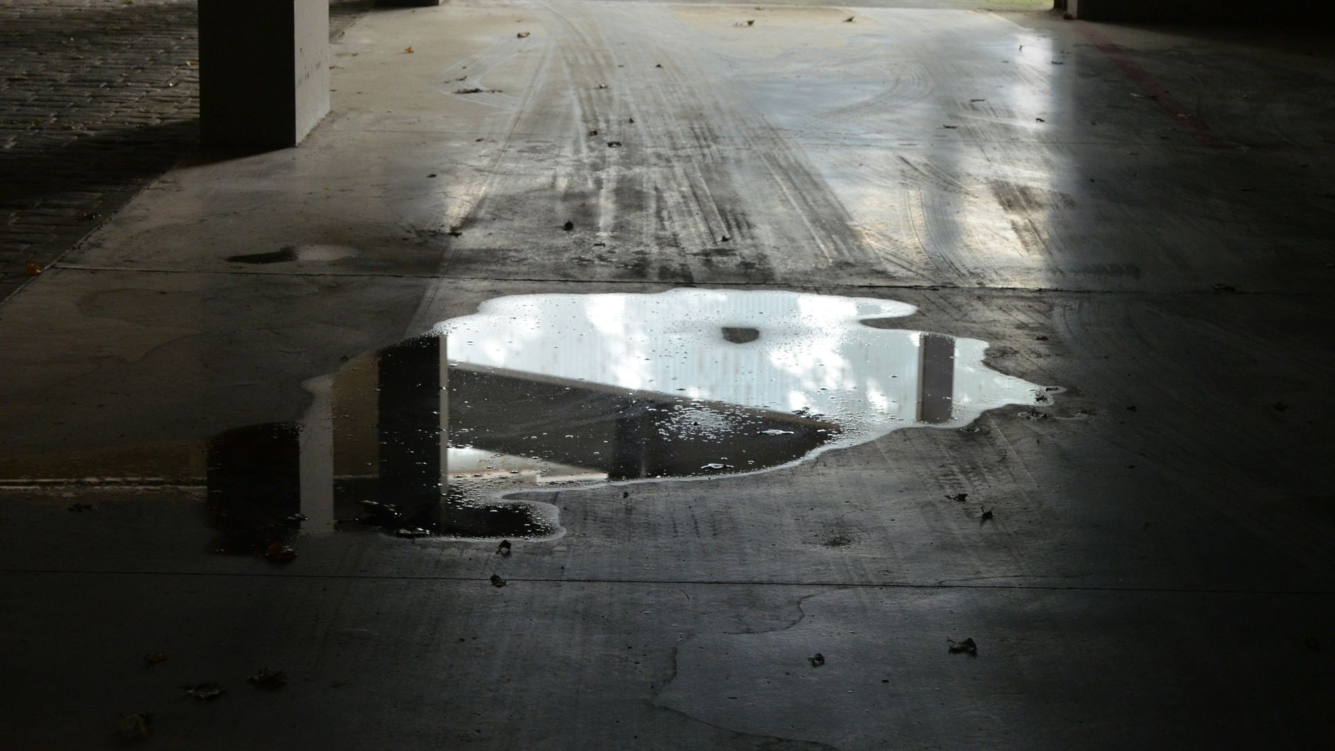 Puddle of standing water on a concrete slab with tire tracks, a common sign of poor driveway slope and drainage