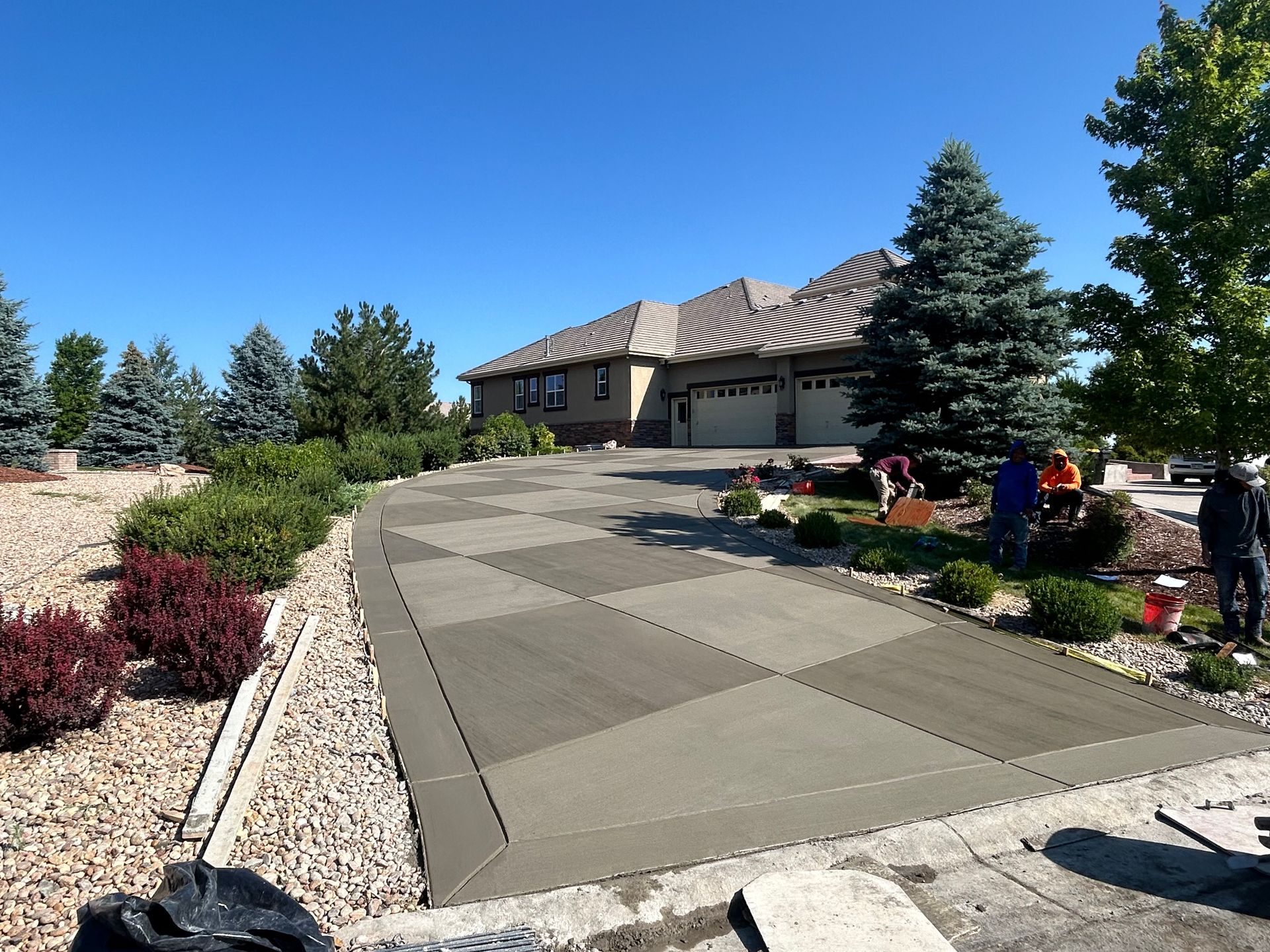 Freshly finished checkerboard-pattern concrete driveway leading to a modern stone-front home in Castle Rock