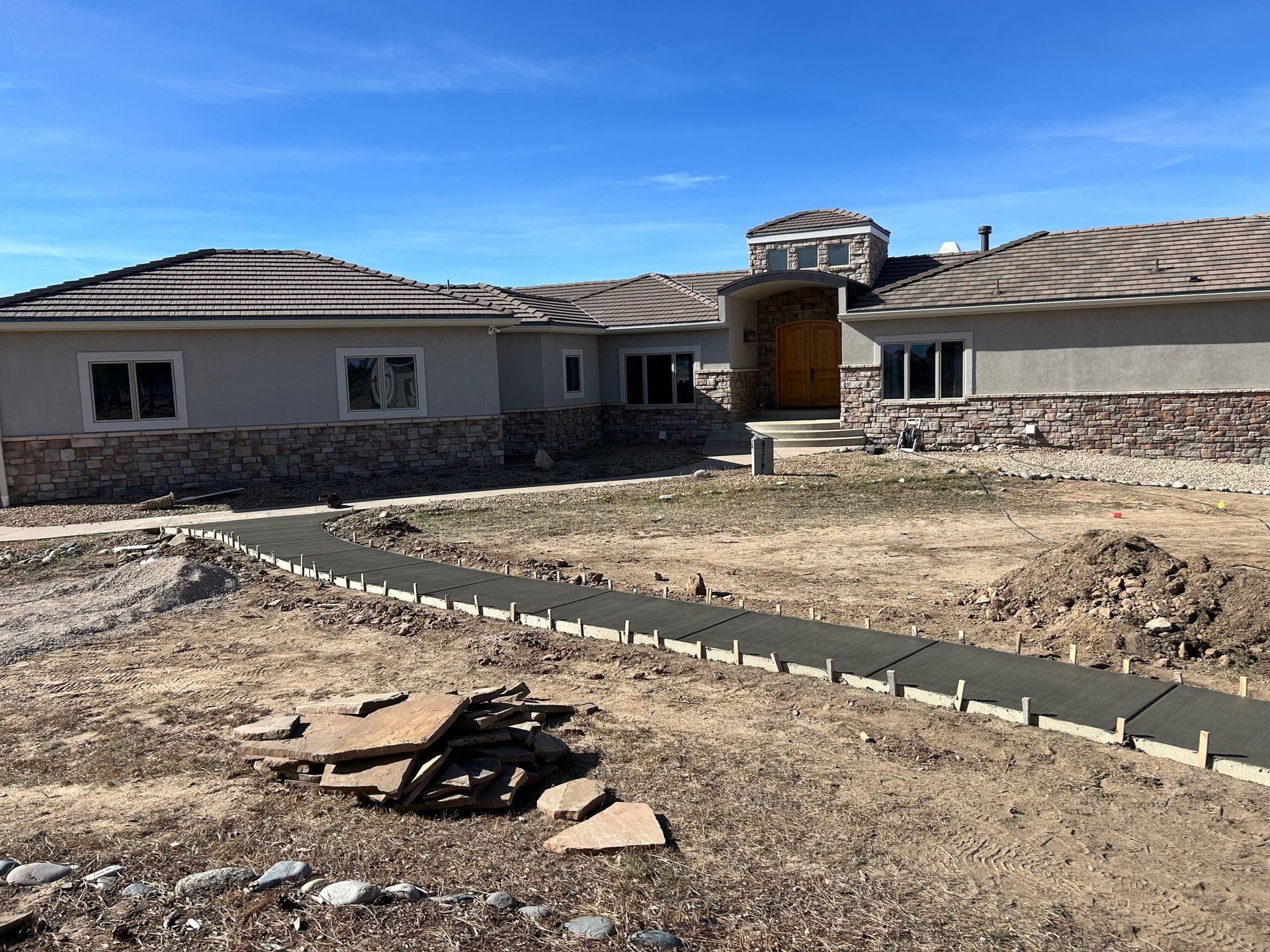 Single-story house under construction with stone facade, unfinished yard, and clear blue sky