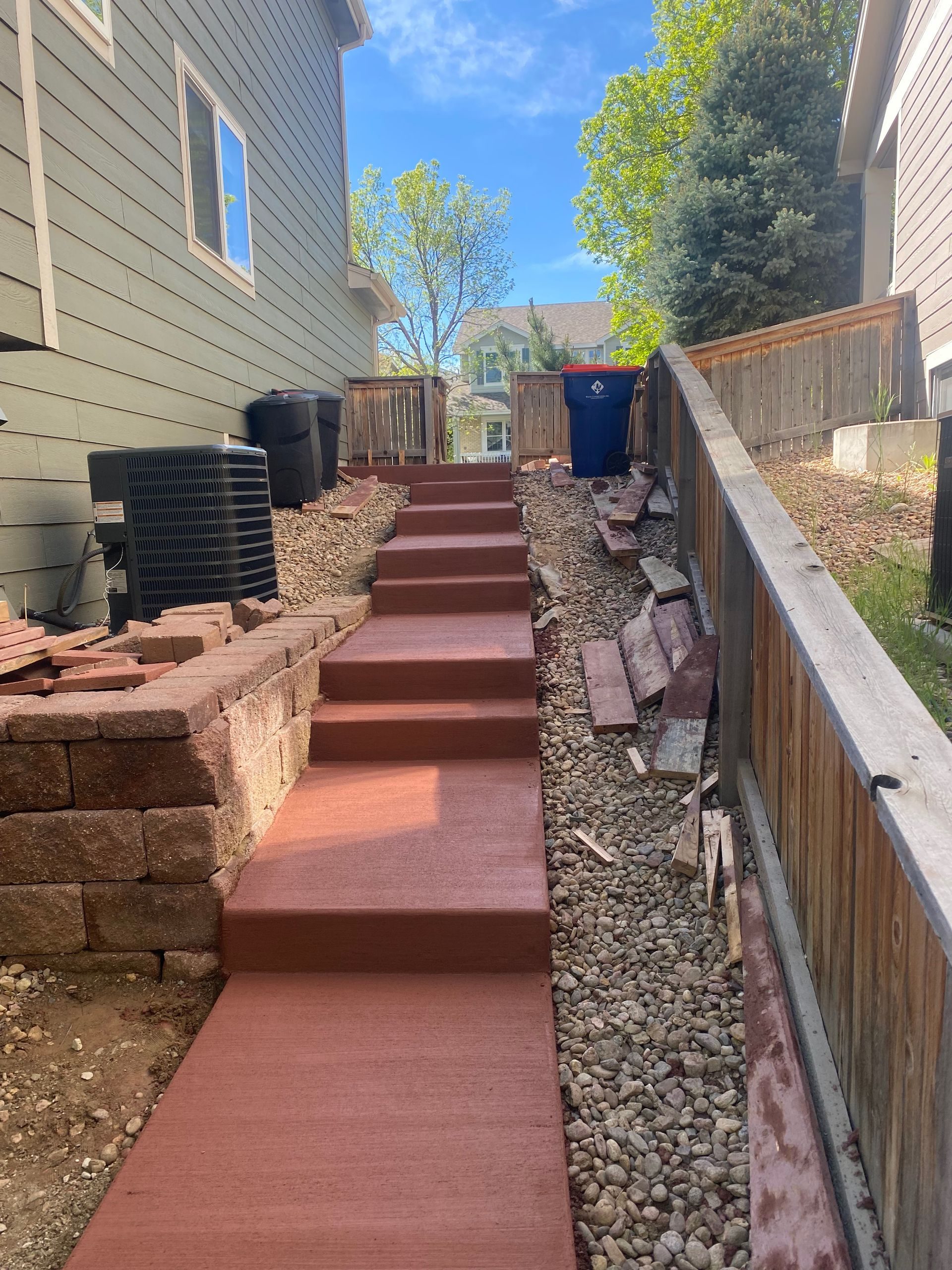 Steep outdoor walkway with red steps between houses, lined with rocks and retaining walls